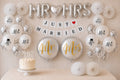 Bruiloftversiering met zilveren MR en MRS letterballonnen, een Just Married slinger, witte ballonnen, pompoms en een bruidstaart.