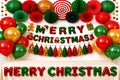 Kerstversiering in rood, groen en goud met Merry Christmas slingers, ballonnen, lampionnen en waaiers boven een crèmekleurige tafel.